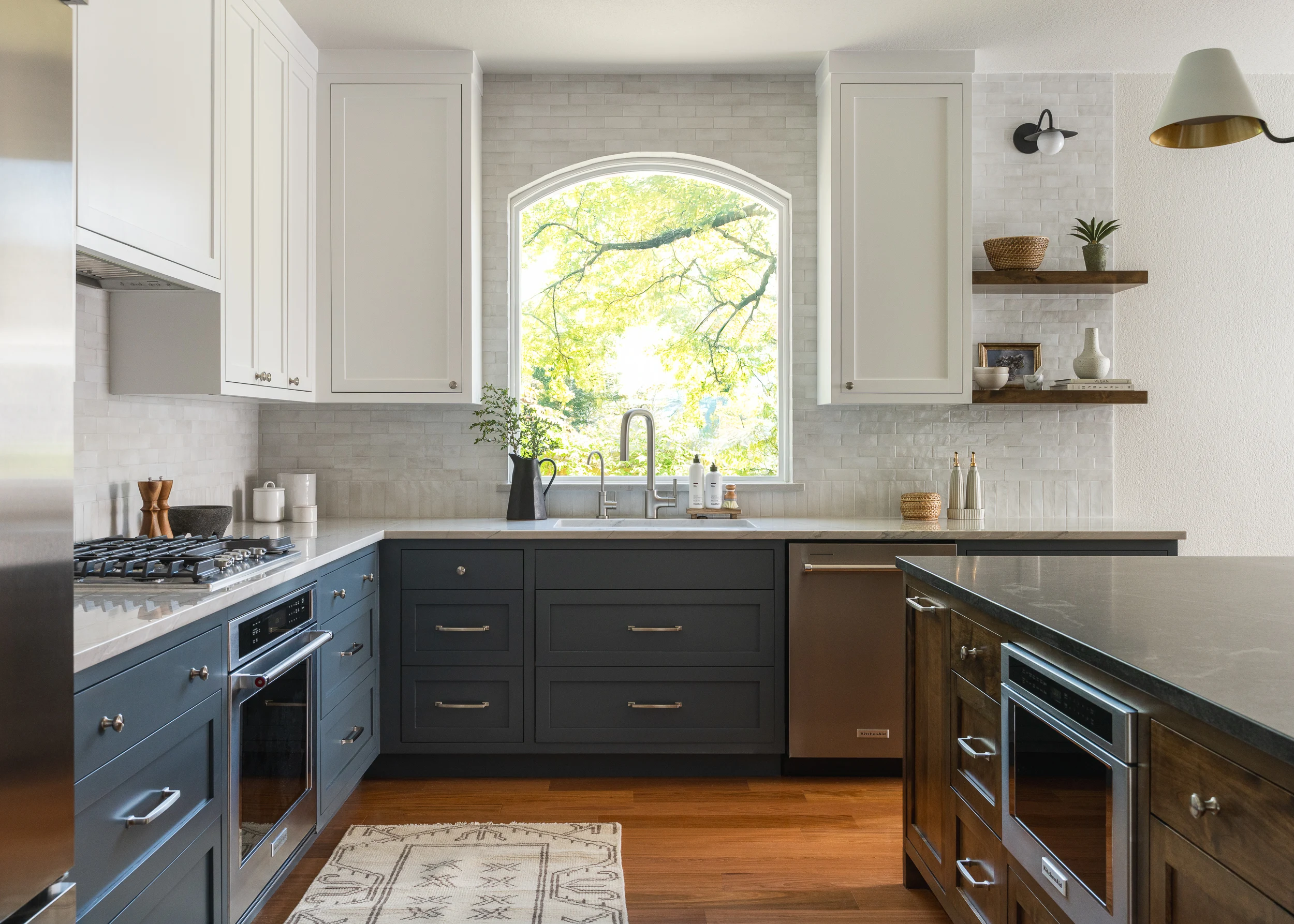 Sink run beneath an arched window, with dark base cabinets and a light quartzite counter