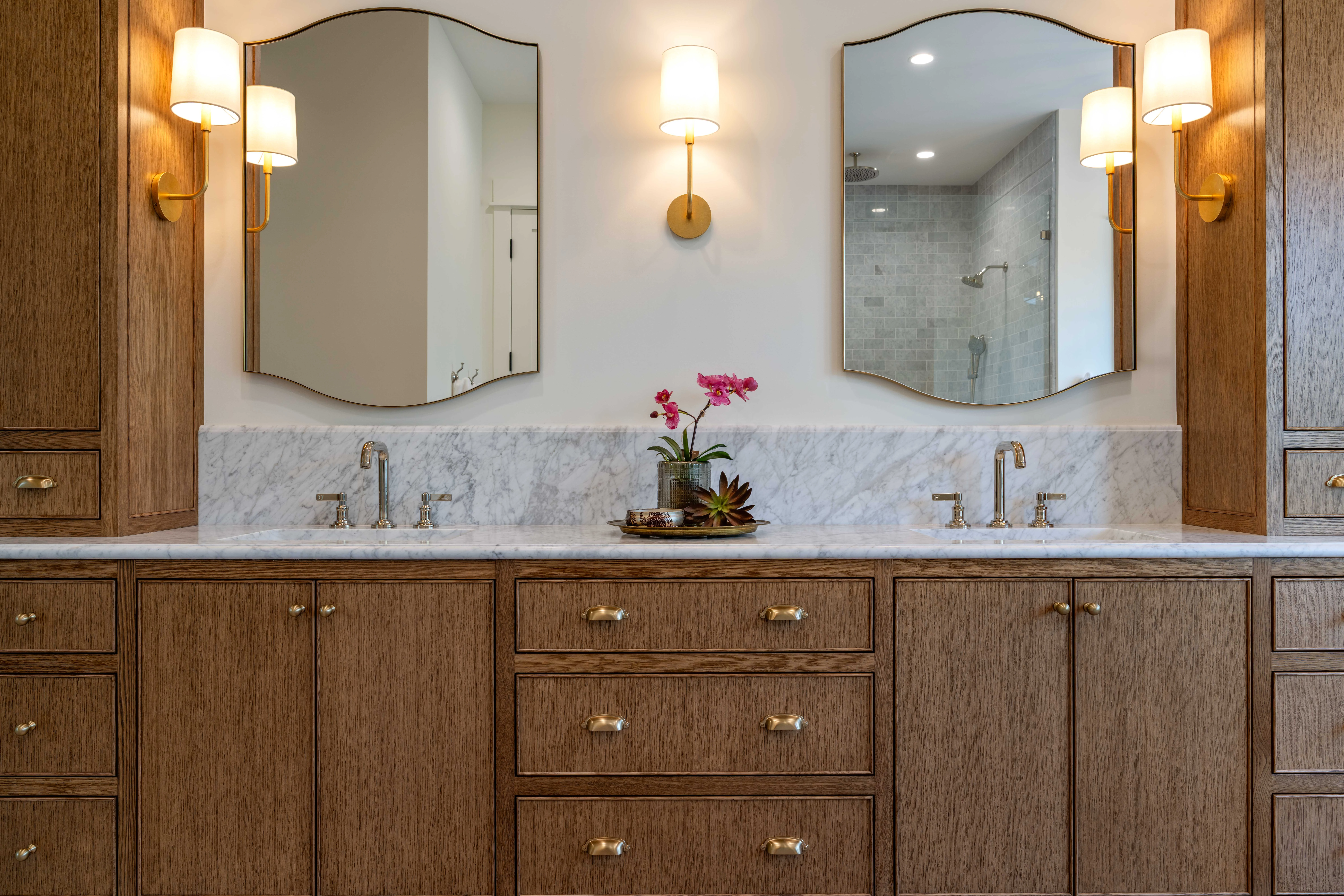 Oak double vanity under arched mirrors and sconces