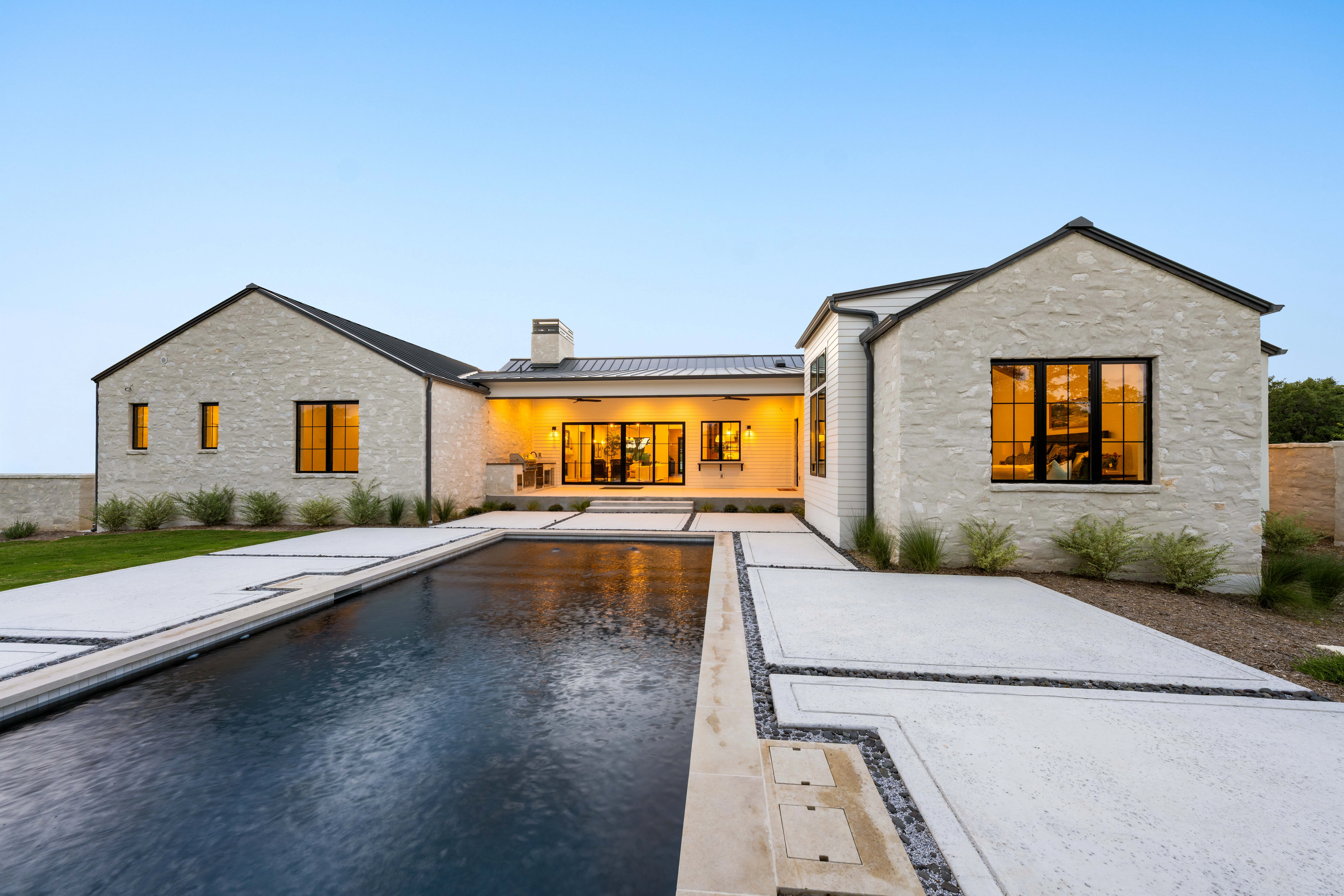 The house lit at dusk across the pool