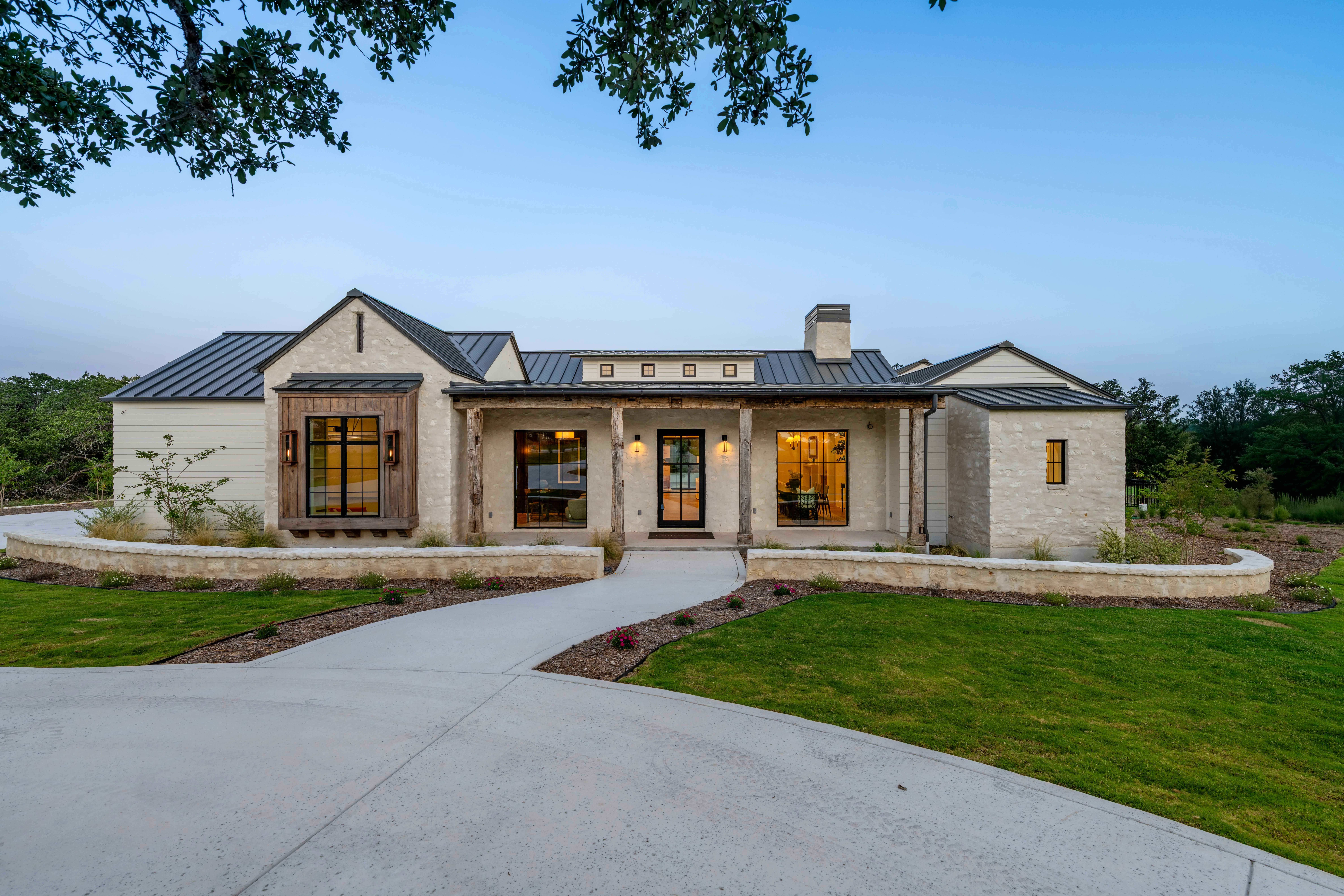 Limestone Hill Country house at dusk, its windows lit, seen up the drive