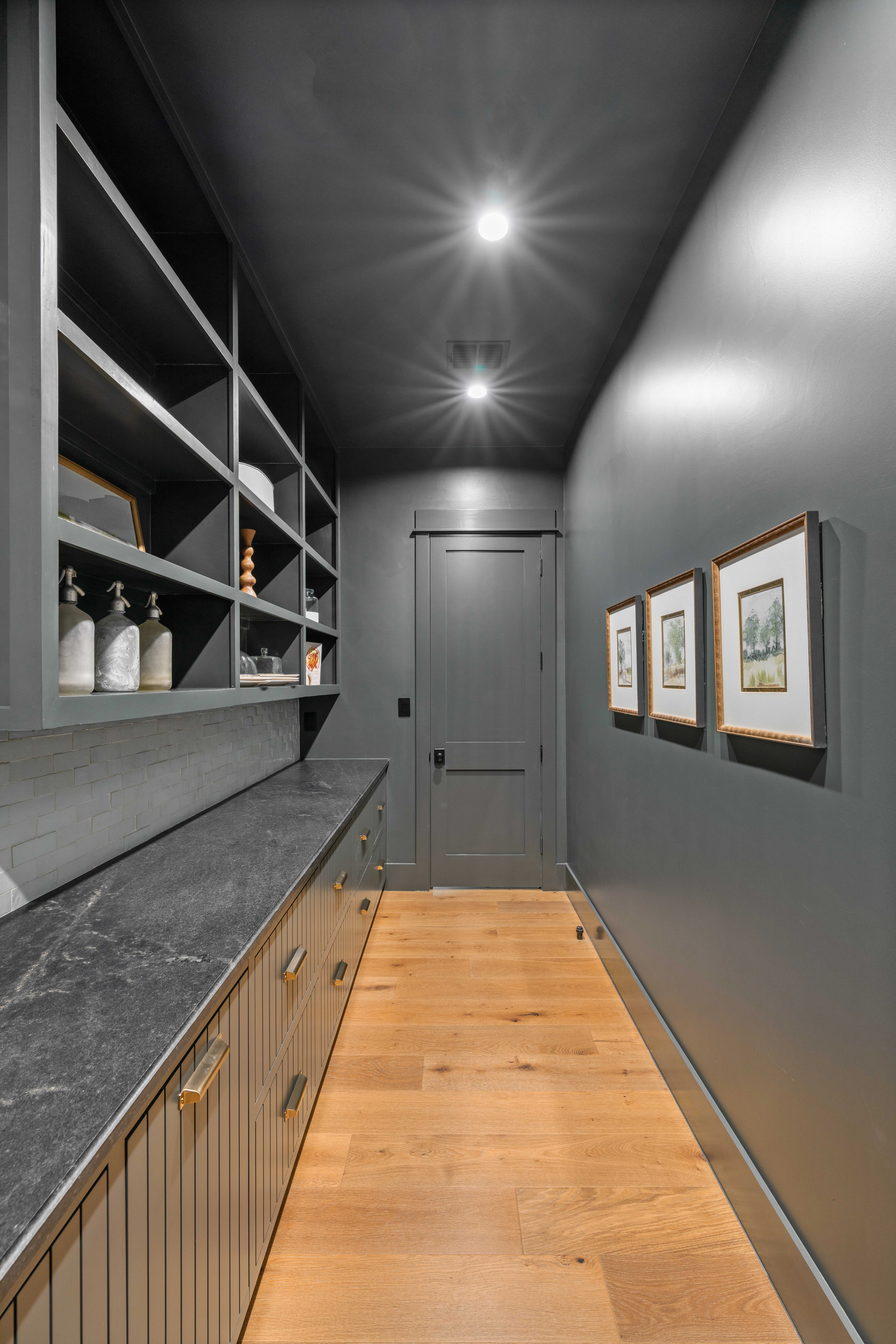 Charcoal pantry corridor hung with framed prints above an oak floor