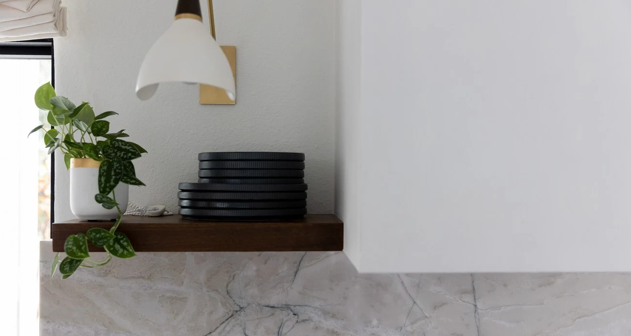 Stacked black plates on a walnut floating shelf under a pendant