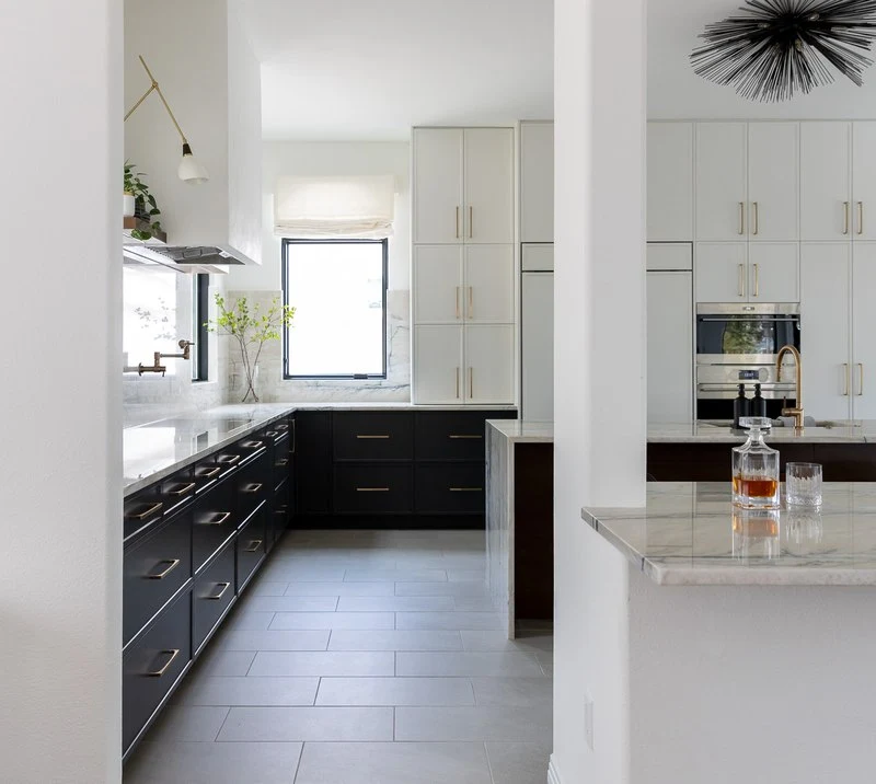 Black lower cabinets and the island seen across the kitchen