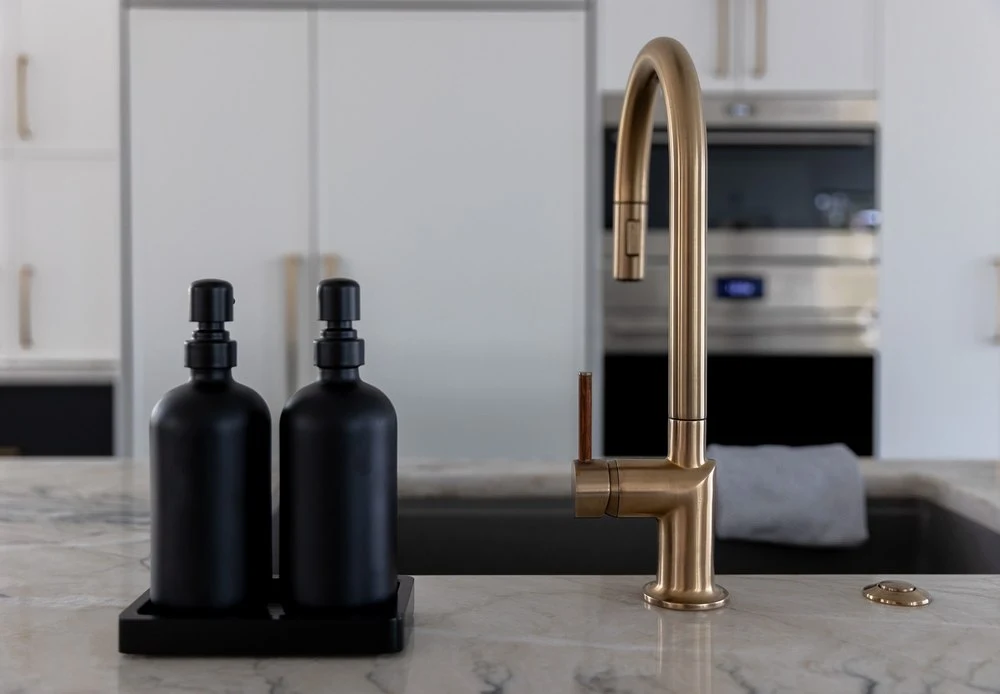 Black soap dispensers beside the gold faucet on the island