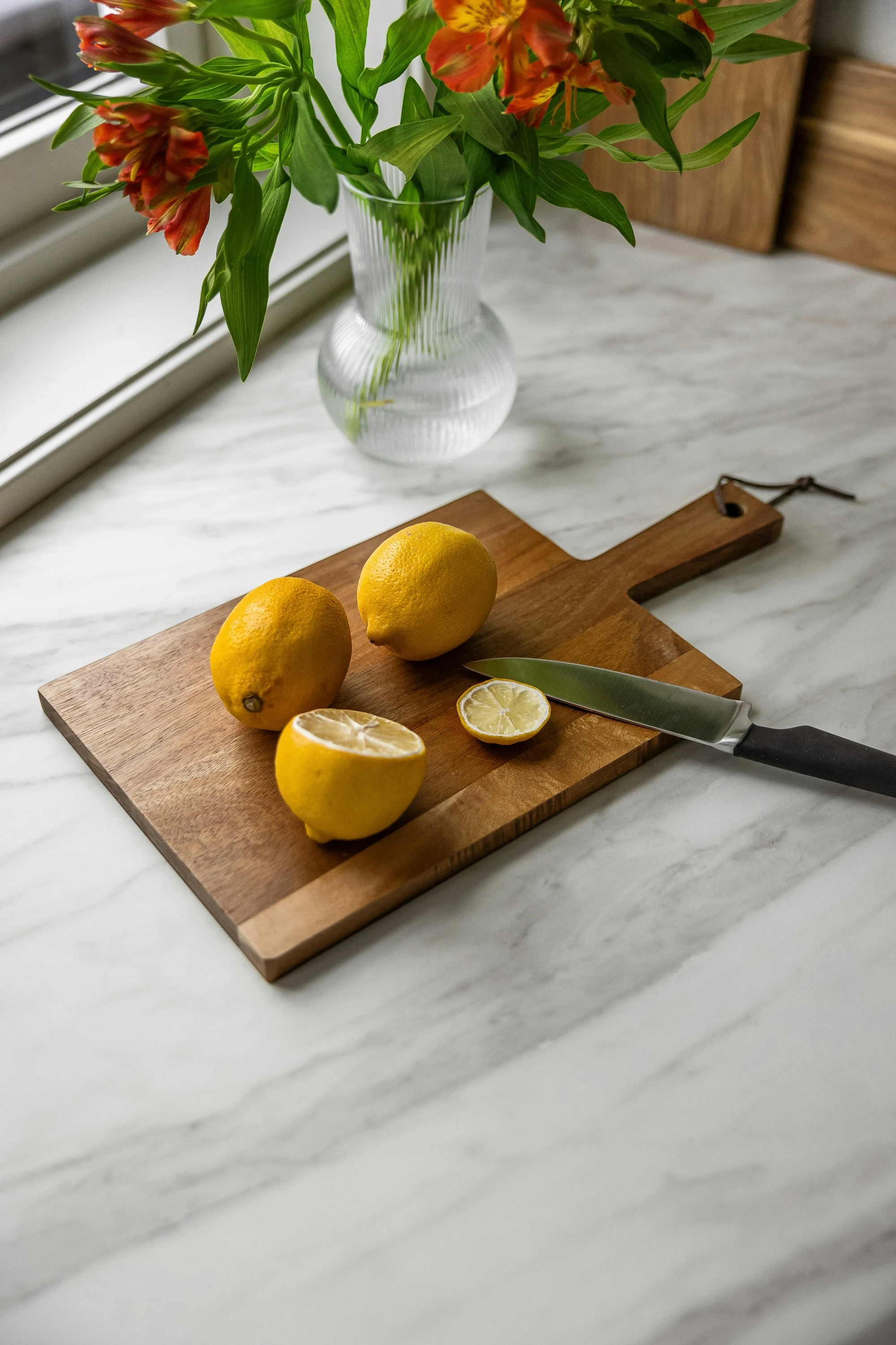 Halved lemons and a knife on a wooden board on a white marble counter
