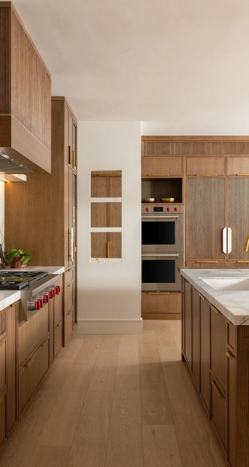 Walnut cabinetry and double ovens down the length of the kitchen