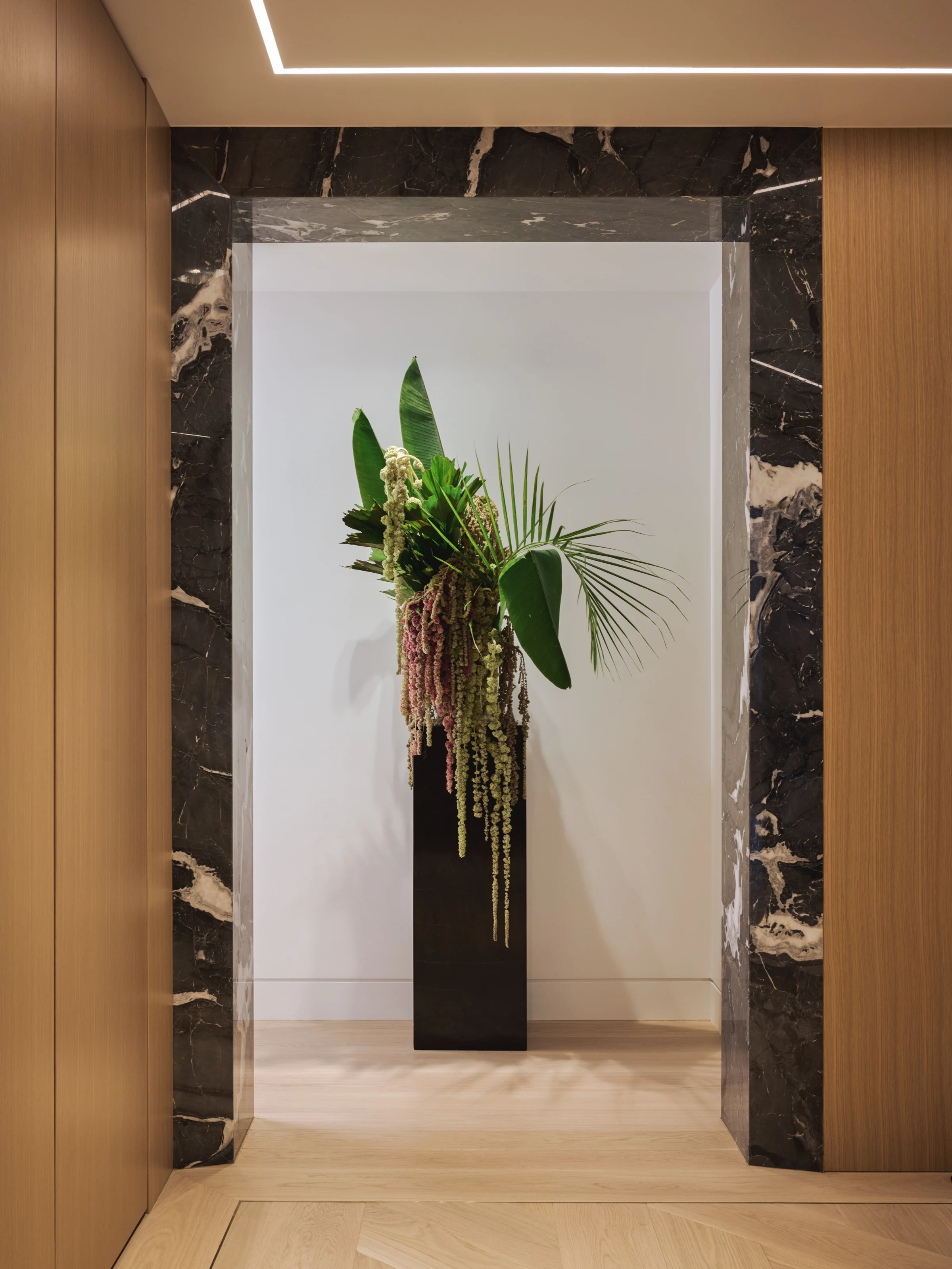 Tall floral arrangement on a black plinth inside a dark marble portal