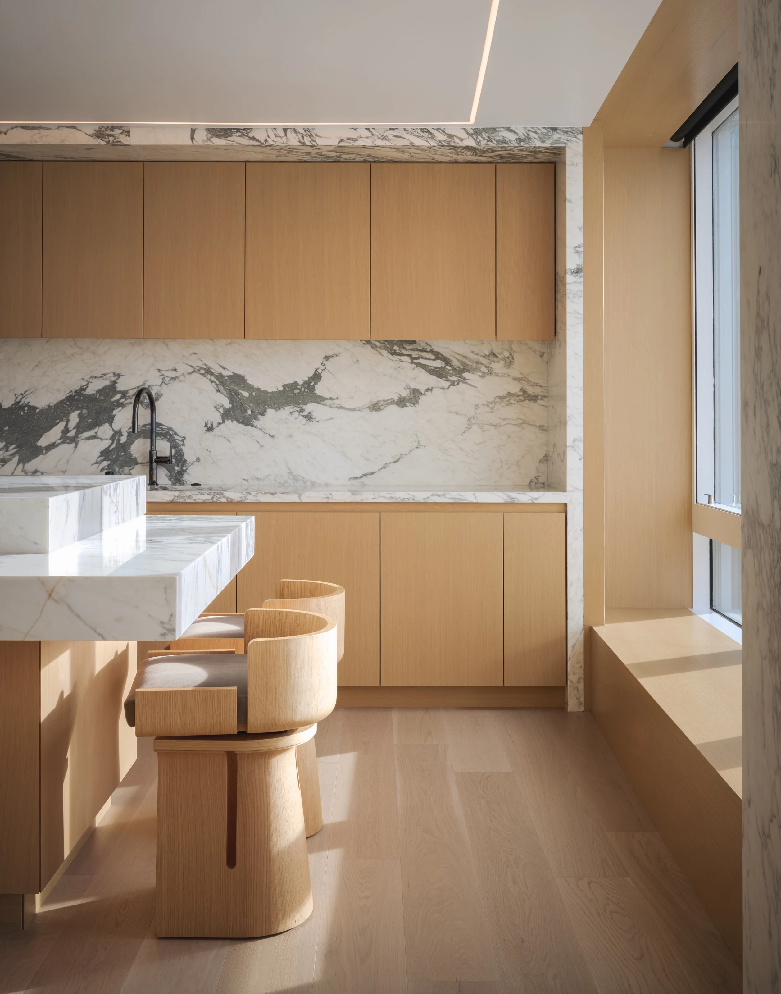 Oak counter stools pulled up to a marble-clad kitchen counter