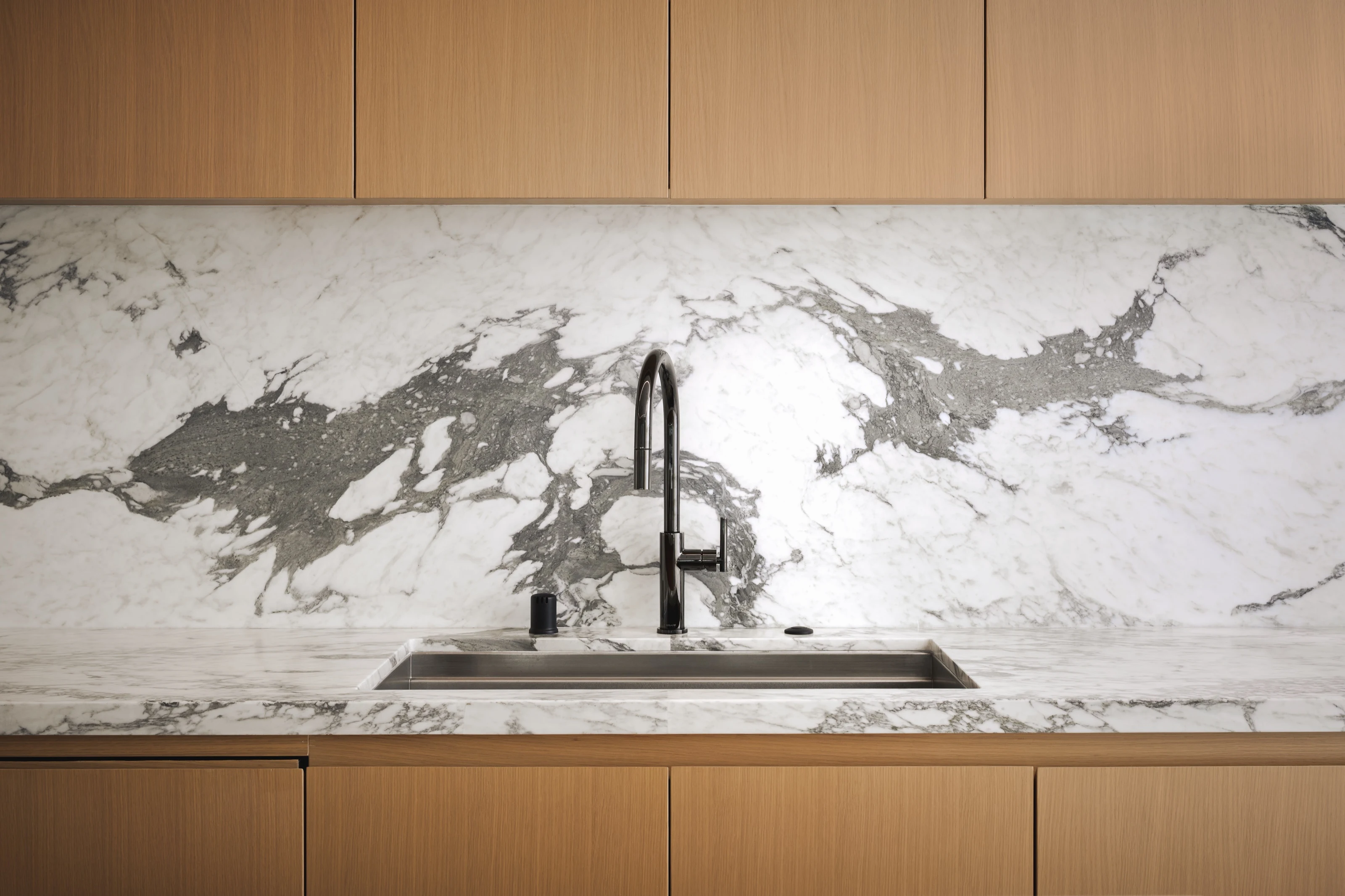 Full-height marble backsplash behind a black faucet and undermount sink