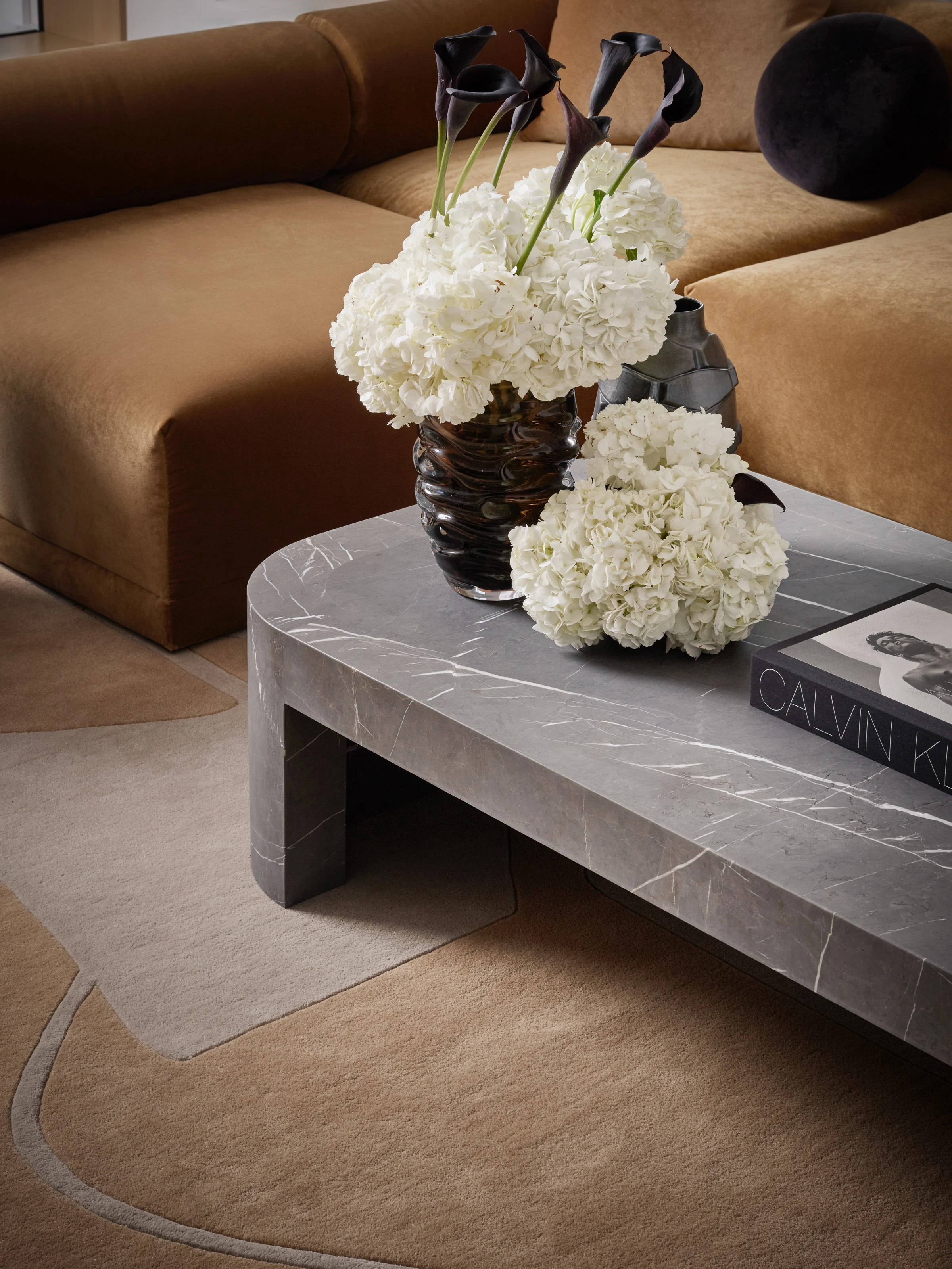 White hydrangeas on a grey marble coffee table before a cognac sofa