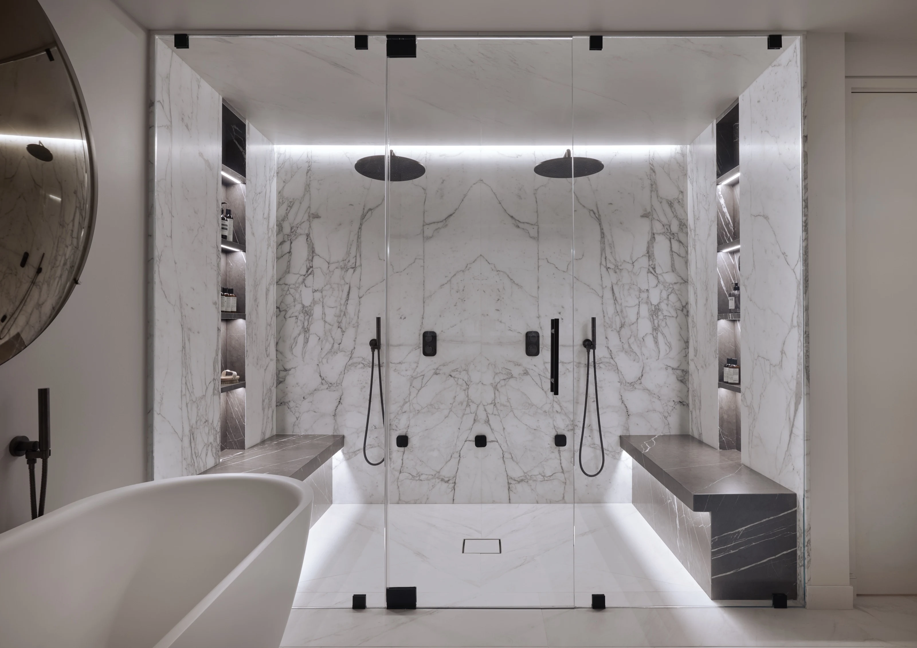 Glass-fronted marble shower with twin rain heads and a lit bench