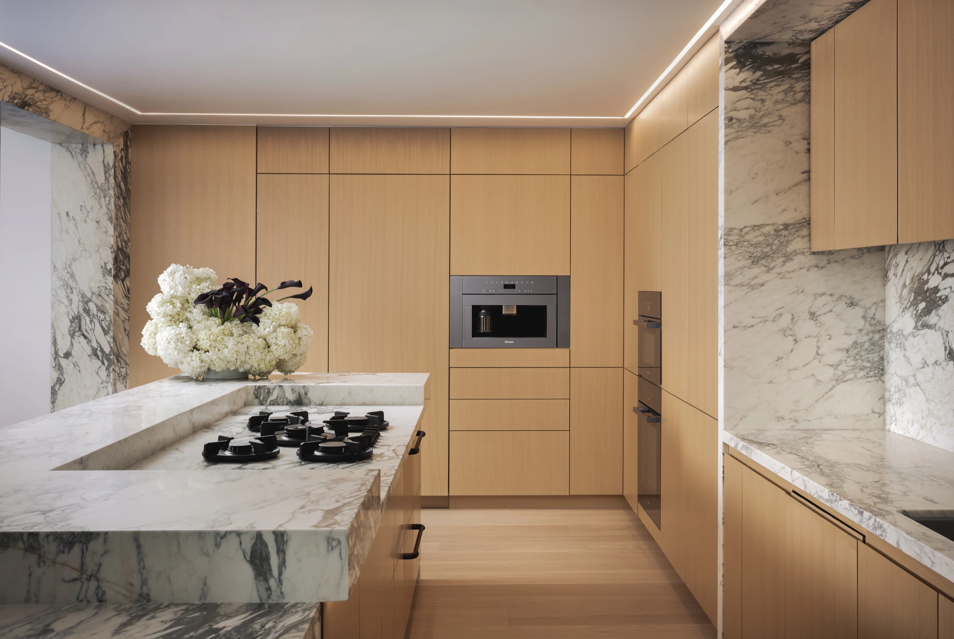 Oak kitchen with a marble-topped island cooktop and built-in coffee machine