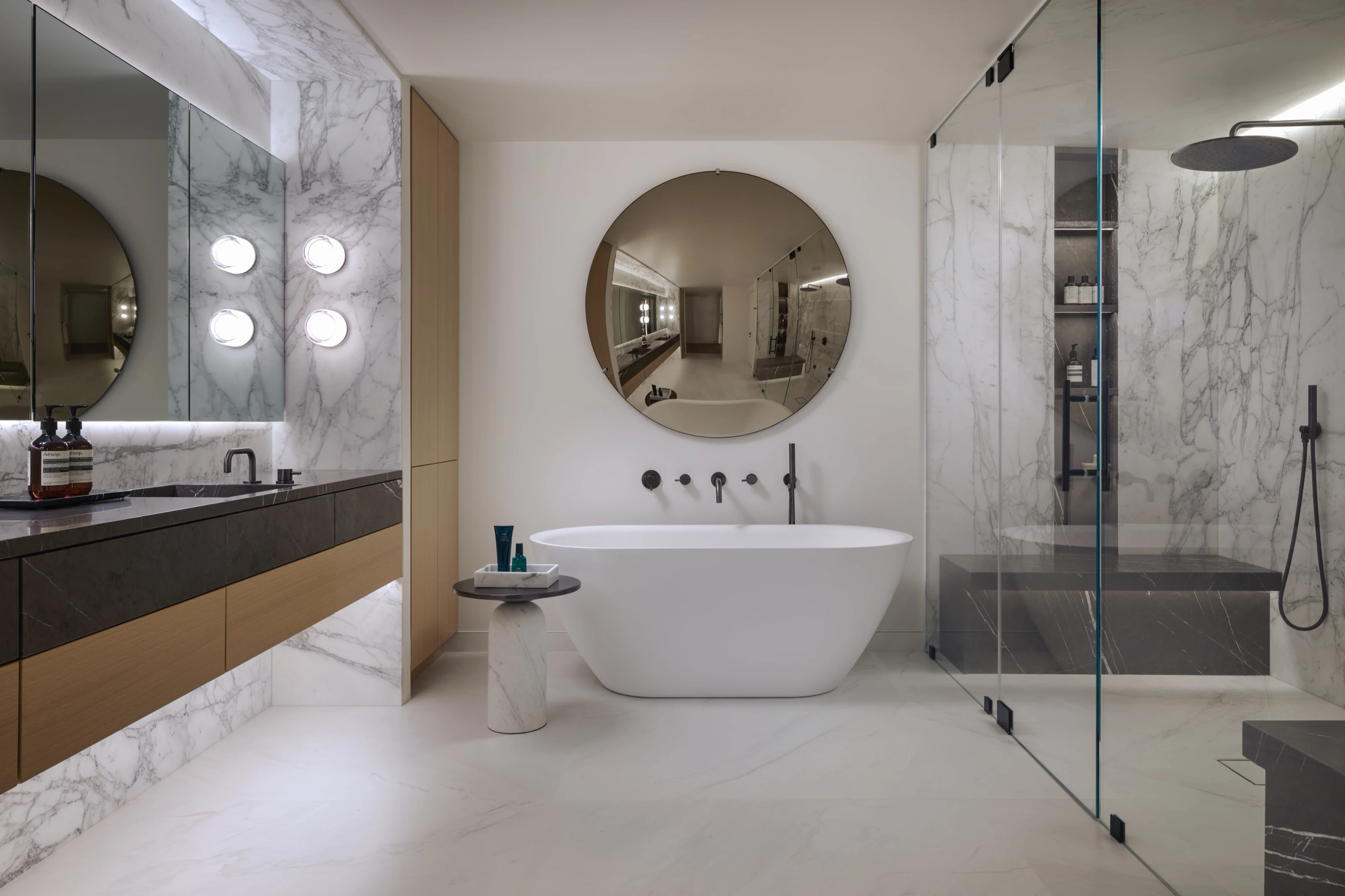 Freestanding tub beneath a round mirror in a marble-lined bath