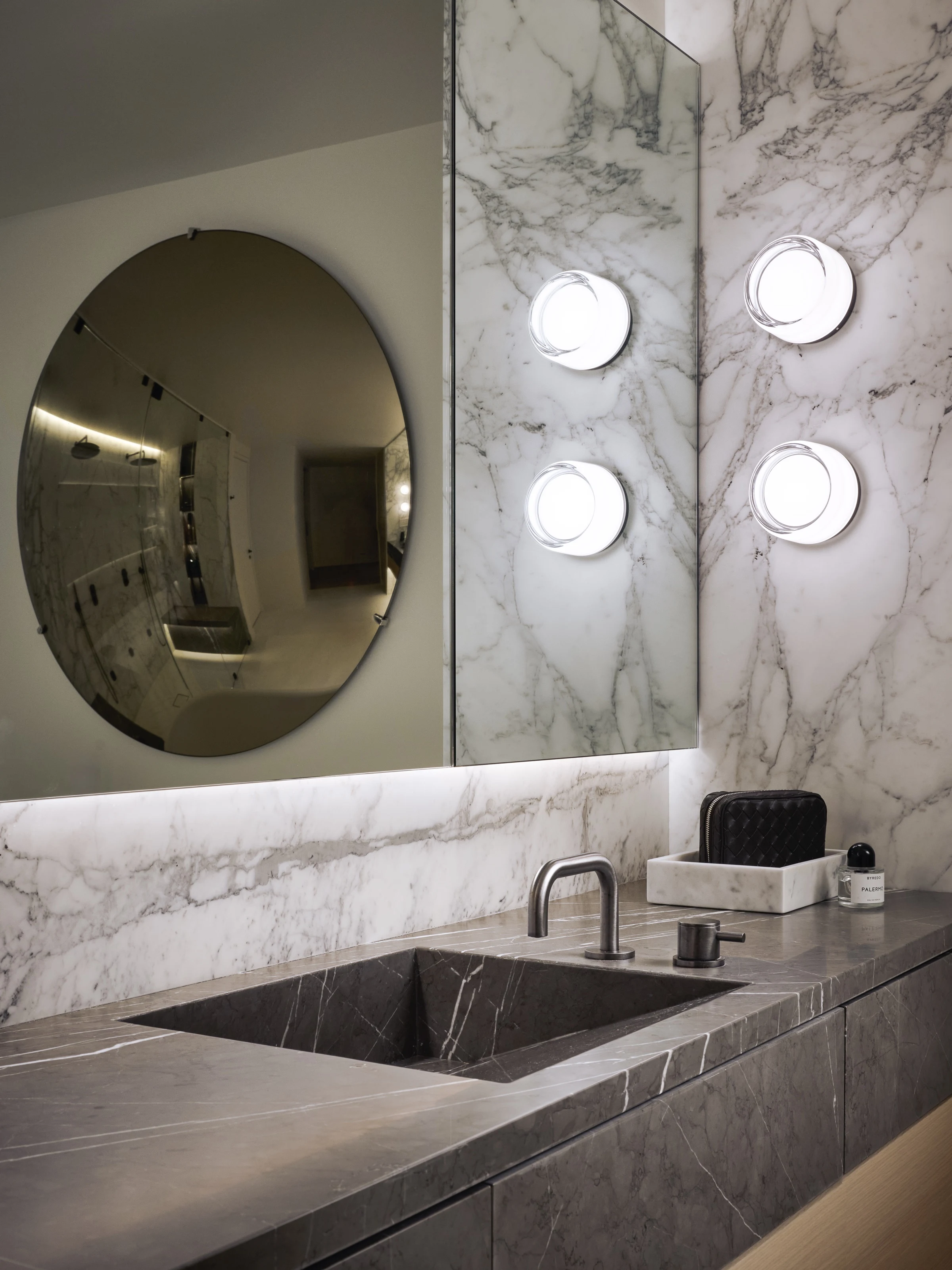 Round mirror and globe sconces over a marble basin