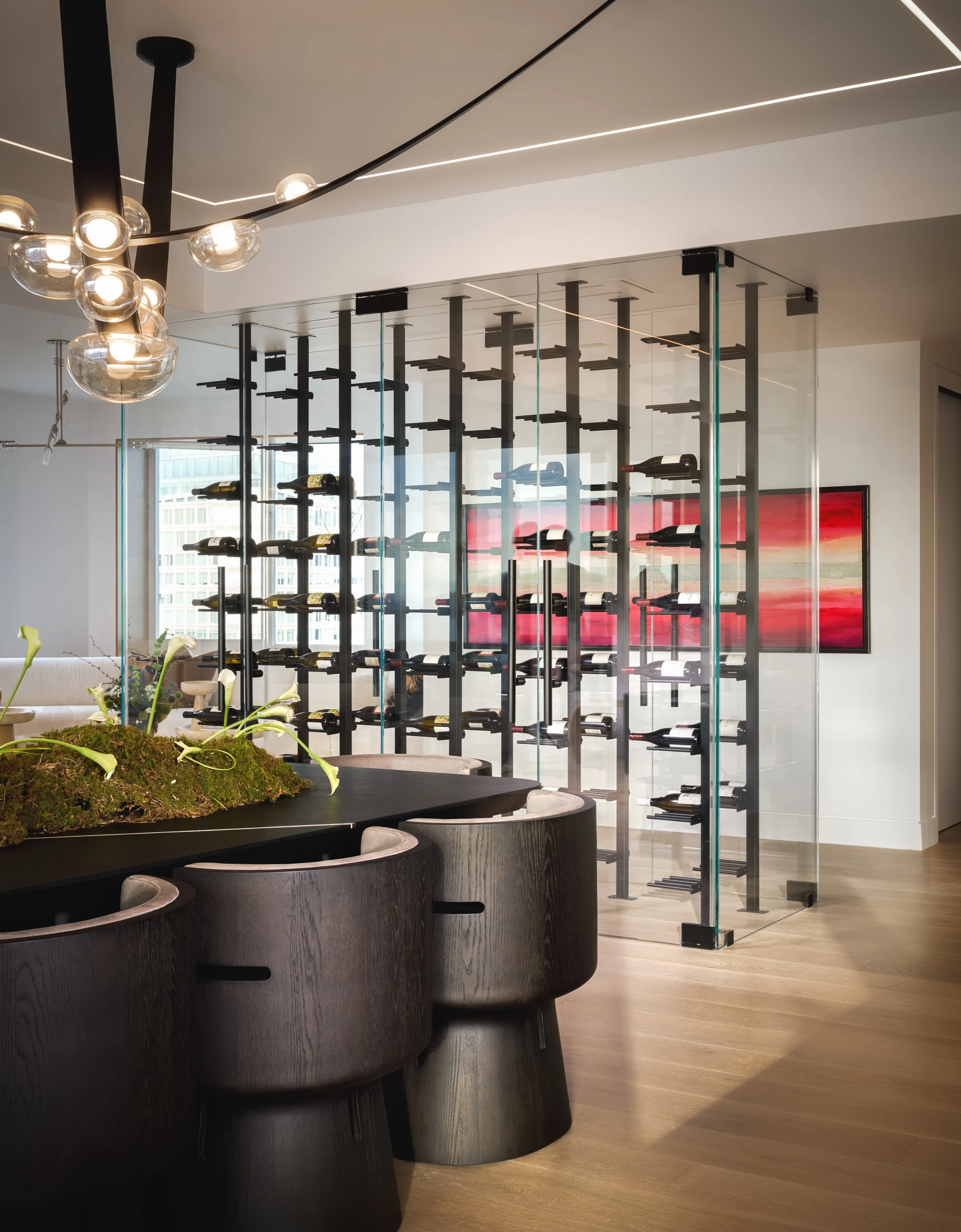 Glass-walled wine room behind the dining table and sculptural chandelier