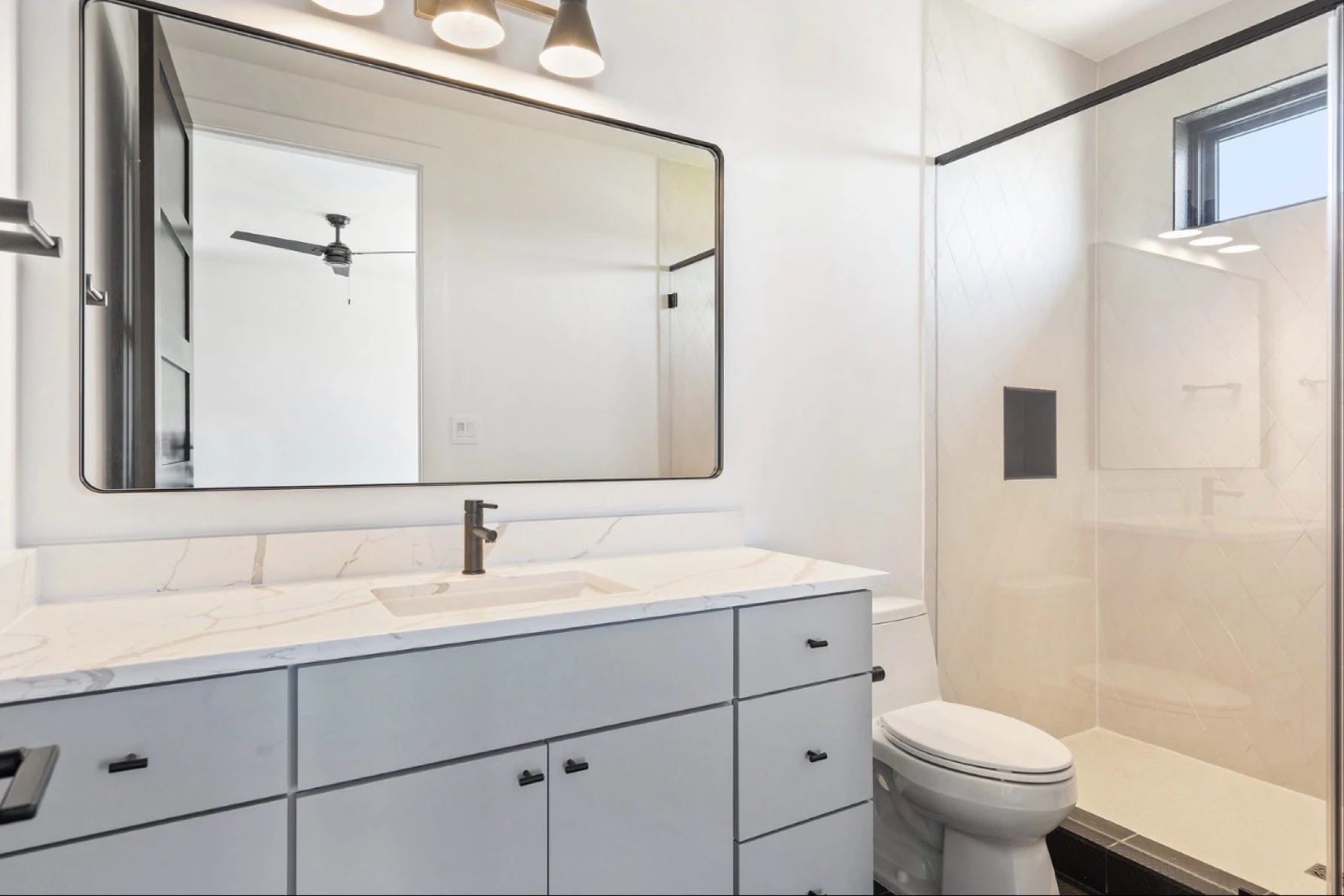 Guest bath before: quartz vanity and a large black-framed mirror