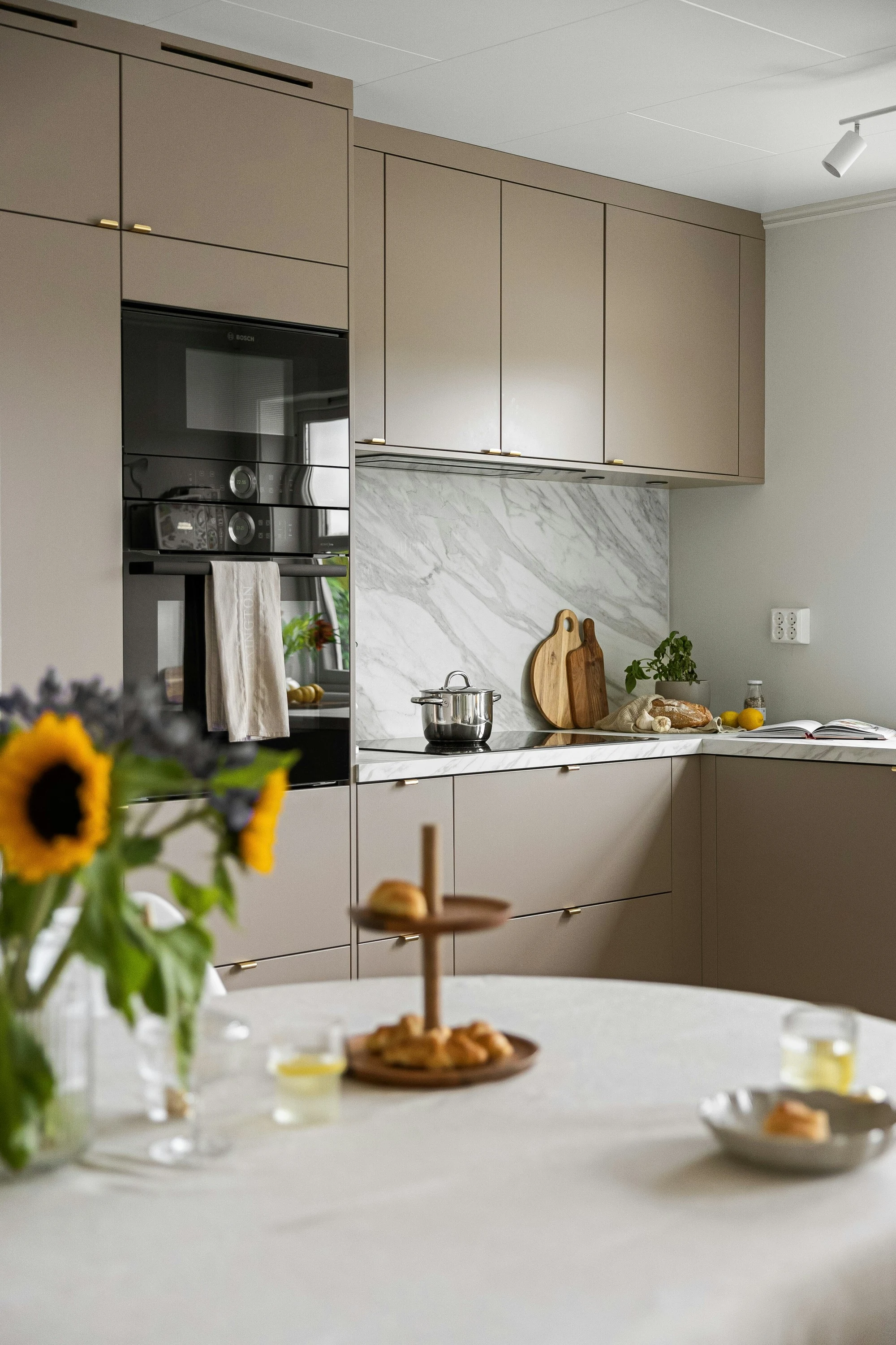 Taupe kitchen with a marble backsplash, and sunflowers on a round table in the foreground