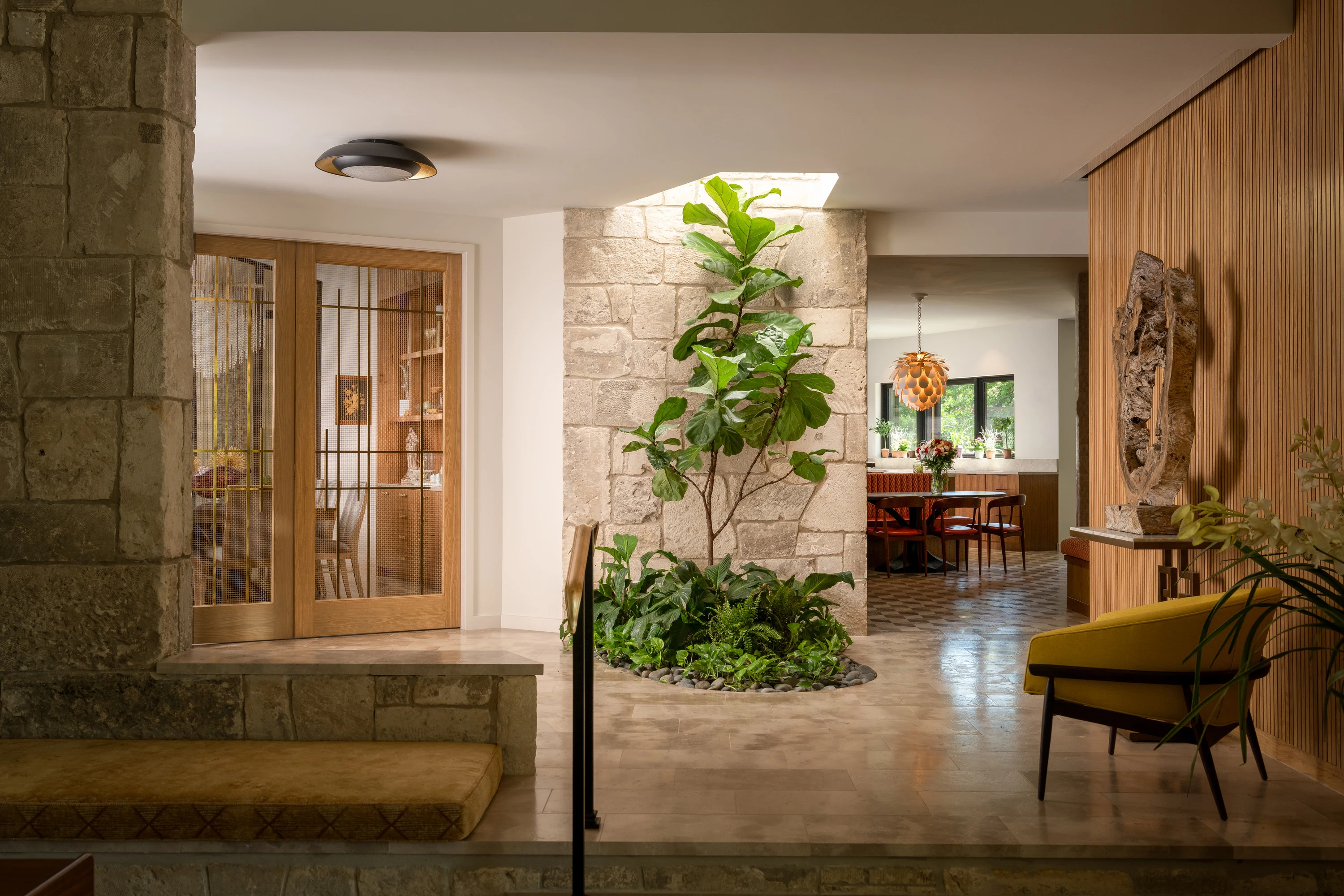 Entry hall in stone and timber opening onto a planted courtyard