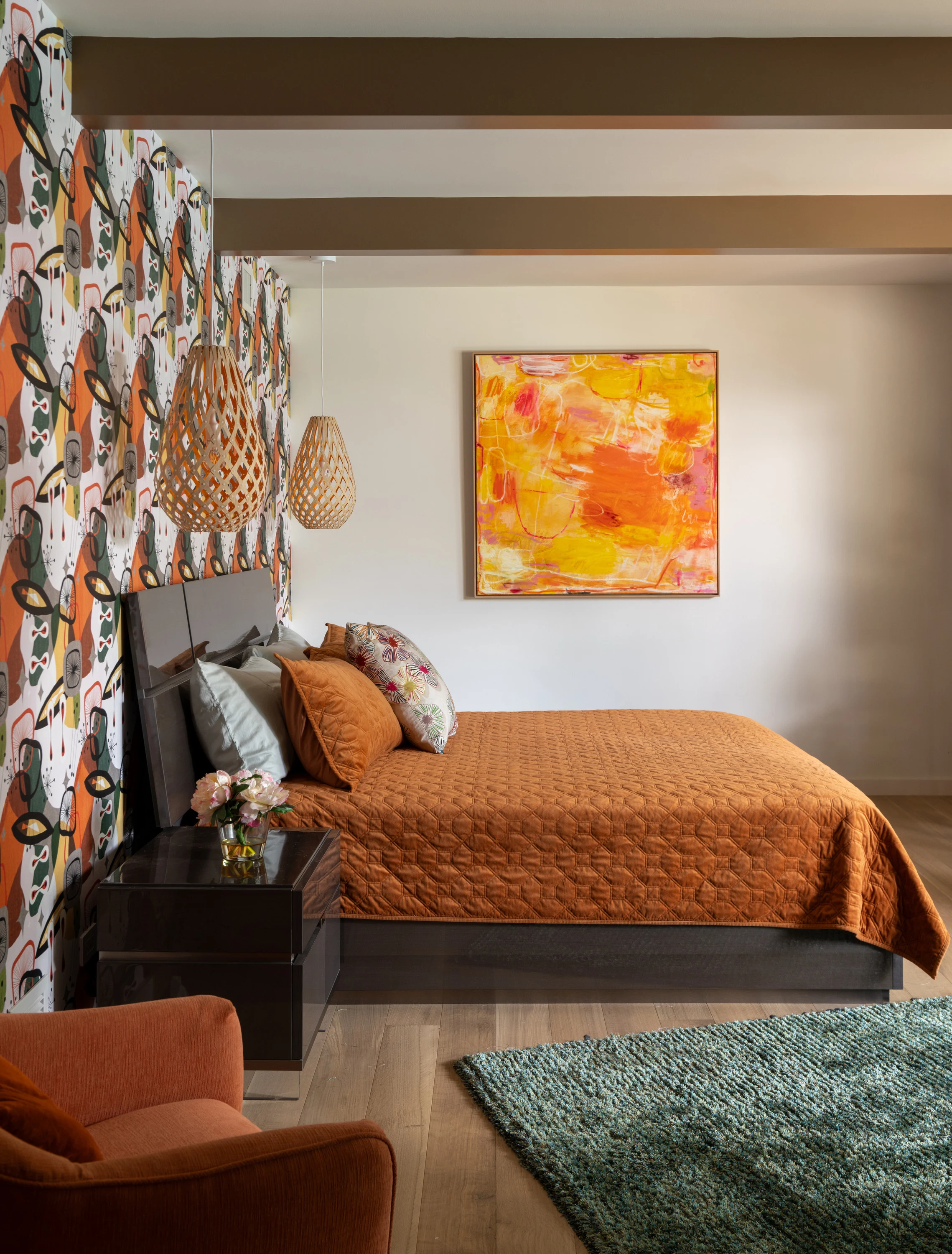Guest bedroom with a rust bedspread, patterned wall covering and bright artwork