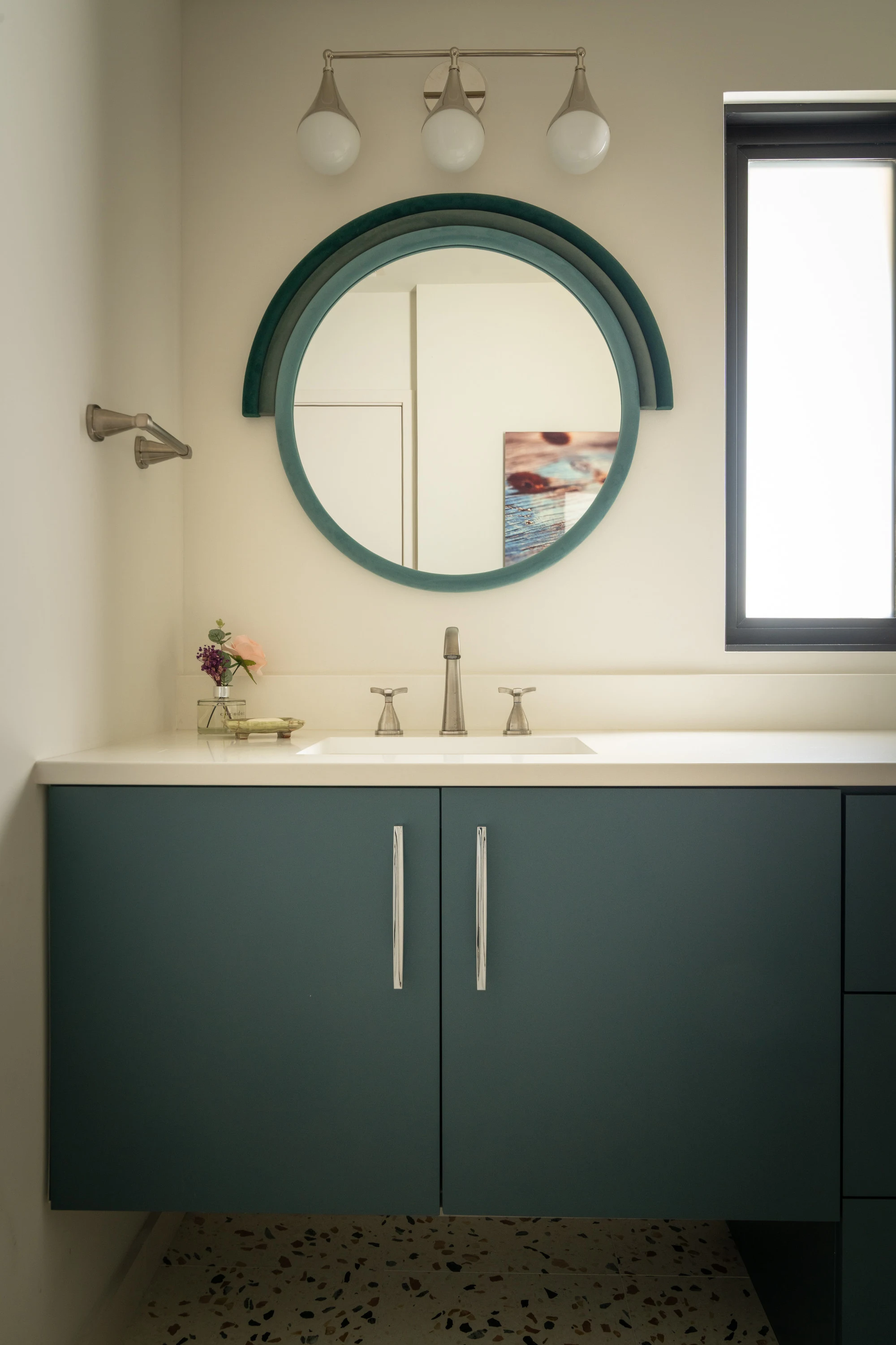 Powder room with a deep green vanity and a round mirror