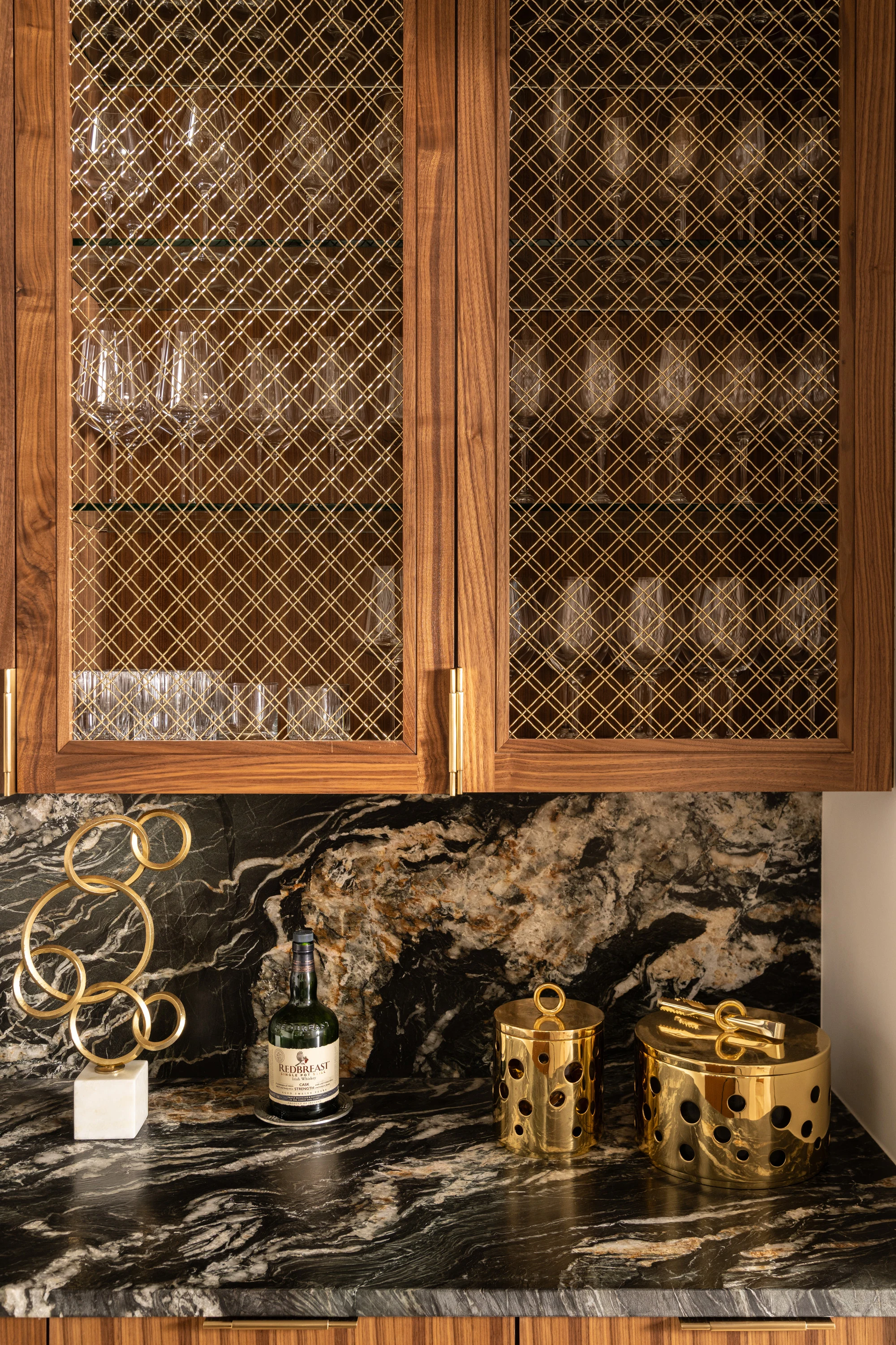Brass glassware on the honed Titanium Granite bar counter beneath mesh-fronted cabinets